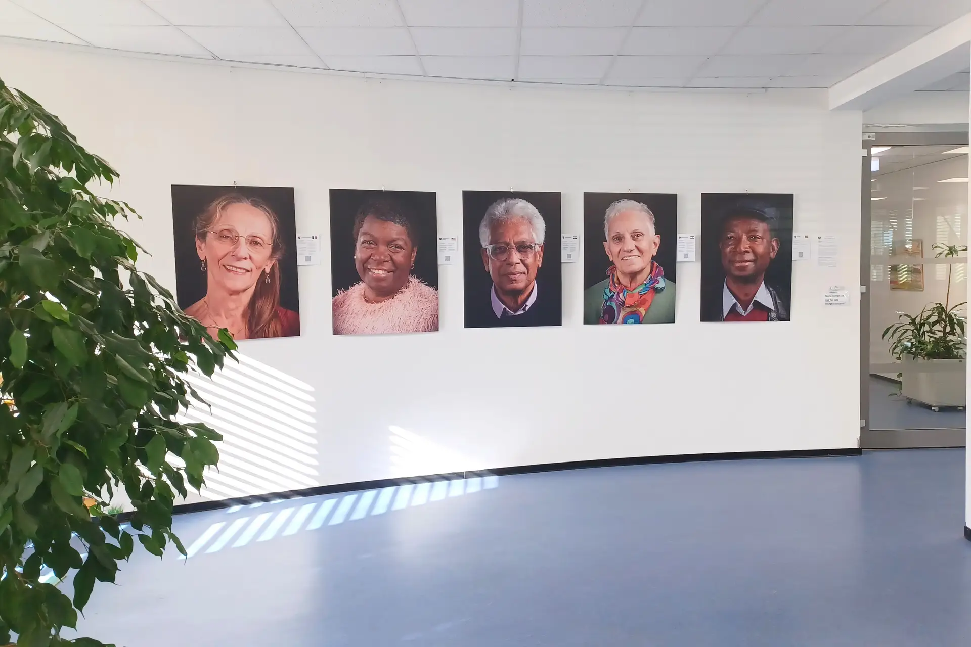 Fünf Porträtfotografien hängen nebeneinander an einer Wand im Rathausfoyer.